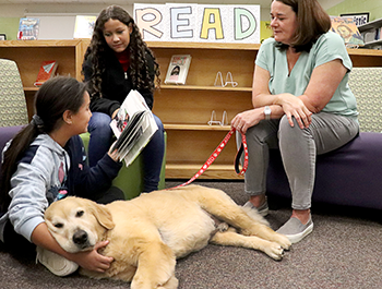 Reggie from the  Alliance of Therapy Dog sitting with students reading in the library